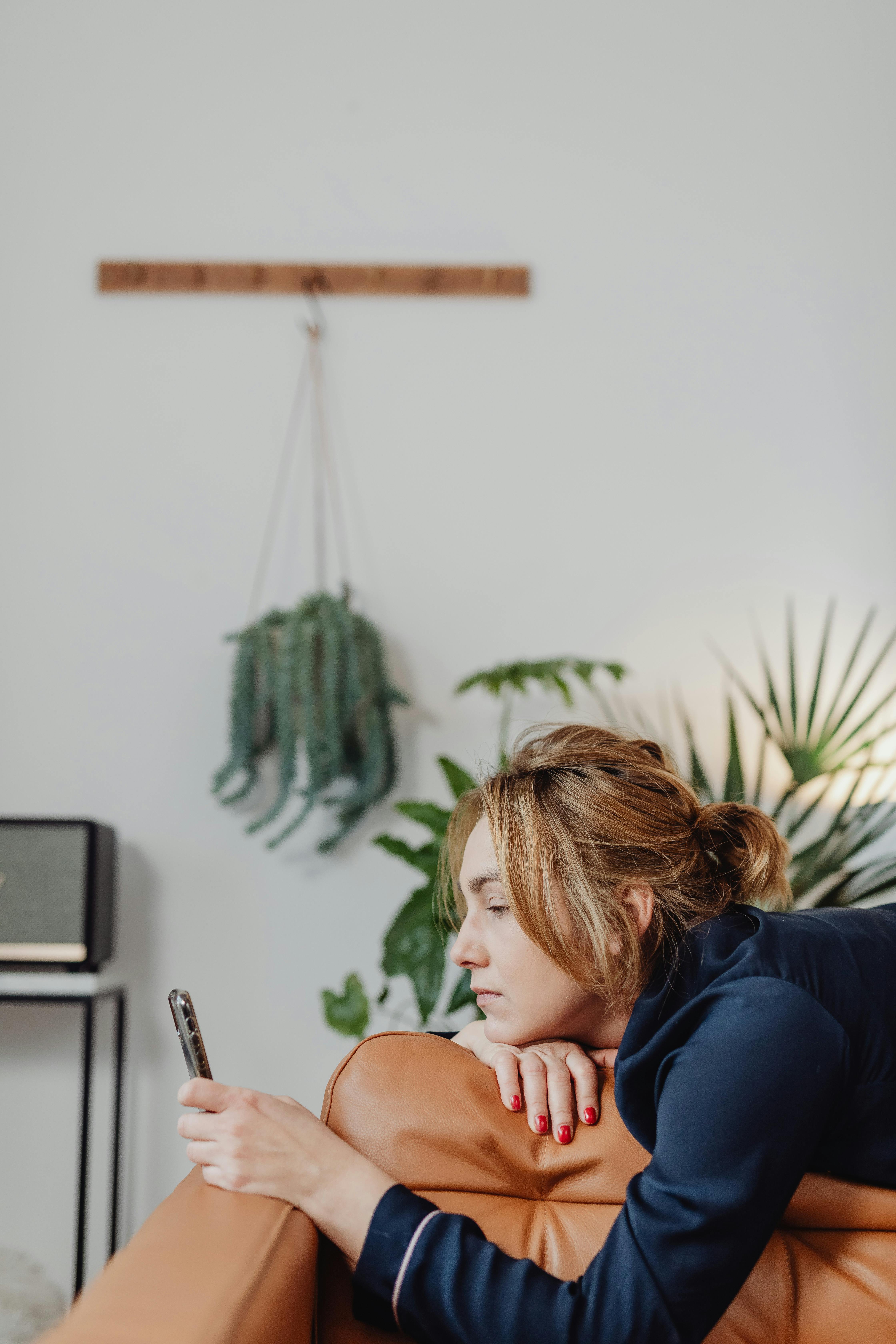 Nő fekszik egy barna bőrkanapén és a telefonját nézi | Forrás: Pexels